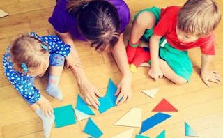 Mother lying on the floor playing with her two kids while folding paper in various shapes and colors