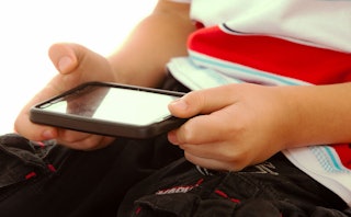 A kid holding a phone in his hands above his lap while  playing games on it