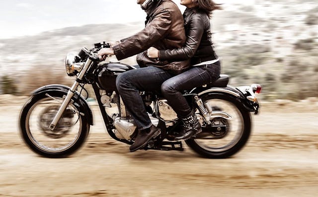 A man in a brown leather jacket and a woman in a black leather jacket riding a motorcycle/blurred du...