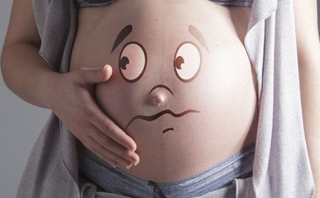 A pregnant woman holding her exposed belly with an illustrated sad-looking face on it