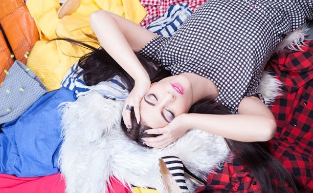 A woman lying on a pile of clothes she'll never wear again with her hands on her head
