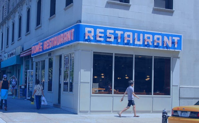 A corner building with a blue 'Restaurant' sign during the day