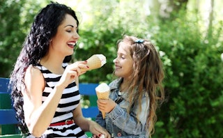 A mother playing with her daughter in a park while both are holding ice cream cones