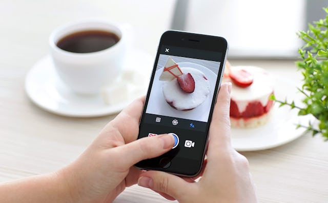 A person taking a picture of a strawberry cake with their iPhone for Instagram