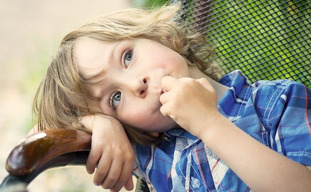 A young blond boy biting his nails