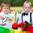 Two young kids sitting at a wedding all dressed up.