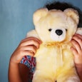 A child hiding behind a teddy bear