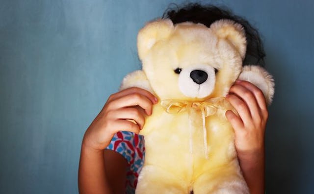 A child hiding behind a teddy bear