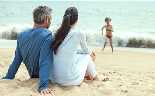 Parents sitting and watching their daughter run towards them at a beach