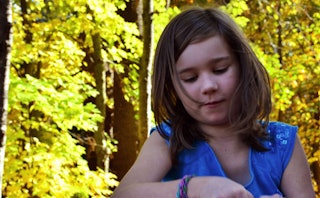 A little girl in a blue shirt in the woods playing reminding her mom she is still a kid