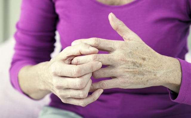 An older woman in a purple sweater holding her left pointer finger with her right hand