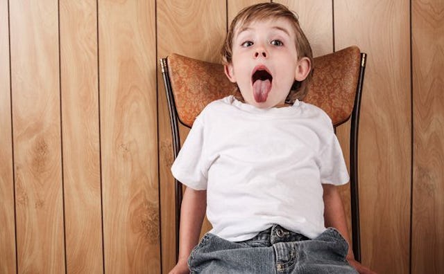 A boy sitting on a chair and sticking his tongue out
