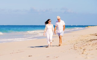 Black-haired woman wearing white clothes holding hands with a man older than her, wearing white shir...