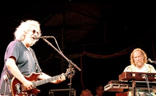 Jerry Garcia playing the guitar and singing next to Vine Welnick playing on the keyboard; they're pe...