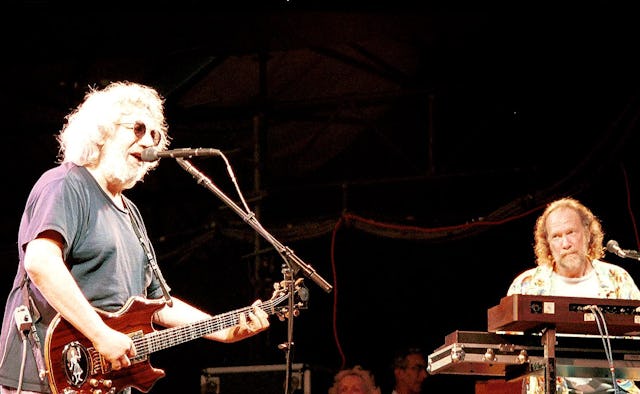 Jerry Garcia playing the guitar and singing next to Vine Welnick playing on the keyboard; they're pe...