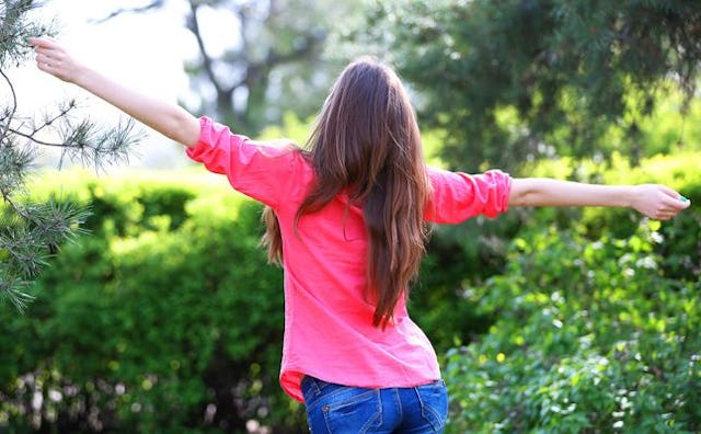 A young mother wearing a pink shirt and blue jeans, enjoying a selfish moment with her arms spread i...