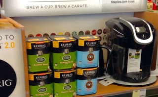 An image of a coffee machine and different flavors of coffee on a store shelf in a dorm room