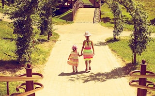An older and younger sister in striped pink and lime dresses with hats walking down the lane decorat...