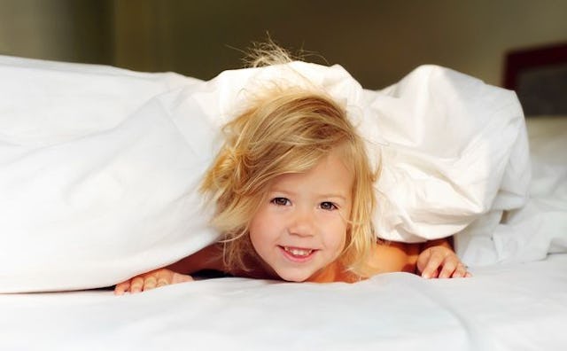A toddler poking their head out of the covers after rising early