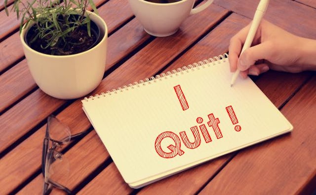 A mother writing a resignation note for motherhood that states 'I Quit!' in red on paper