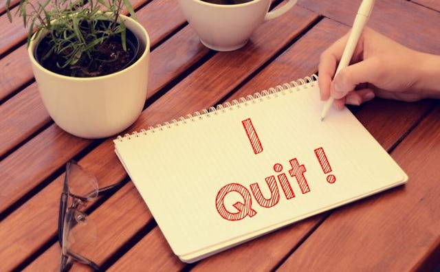 A mother writing a resignation note for motherhood that states 'I Quit!' in red on paper 