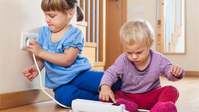 Two kids playing with an electric socket and an outlet power switch in a house