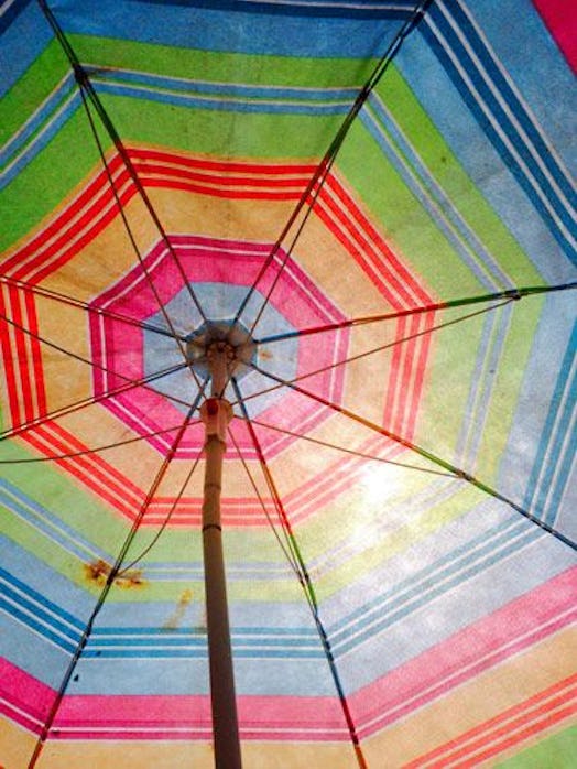 A rainbow sun umbrella at the beach protecting as a Summer's nostalgia factor