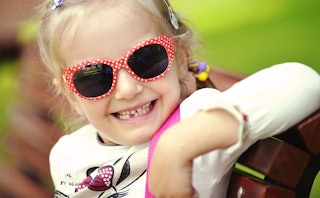 A little girl with polka dot sunglasses smiling after her first lost tooth