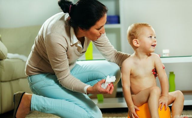 A mum kneeling down next to her baby boy who's on a potty