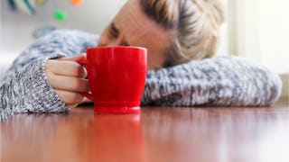 A woman holding a red cup with her head leaning on a table because she needs a break