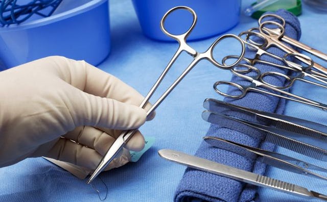 A doctor's hand in a plastic glove with tools needed for a vasectomy
