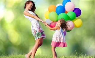 A skinny mom in a white floral dress, grasping her daughters' hands, all the while clutching a bouqu...