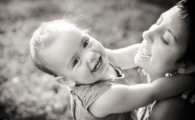 A mother holding her baby son while both are smiling in black and white