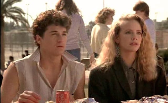 Actors Patrick Dempsey and Amanda Peterson sitting at a table in a scene from the "Can't buy me love...