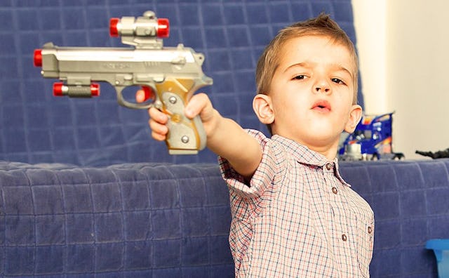 A young brown-haired boy is having a serious face while pointing the pretend gun toward something in...