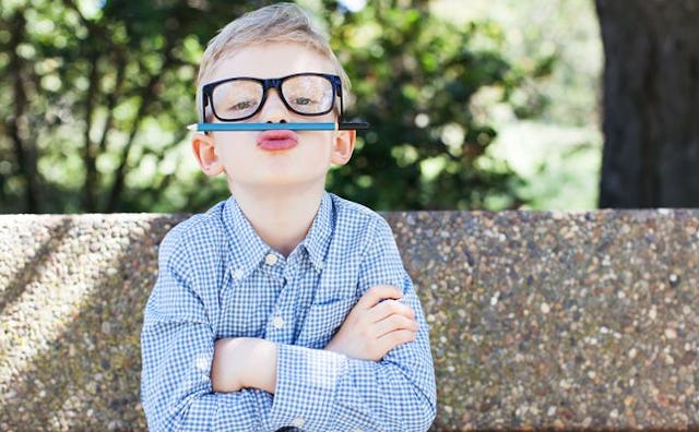 A quirky kid in a blue shirt with glasses holding a pencil with his upper lip as a moustache