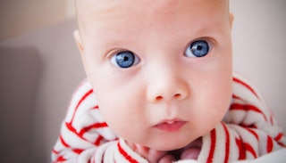 A baby with big blue eyes in a red and white shirt looking at the camera.