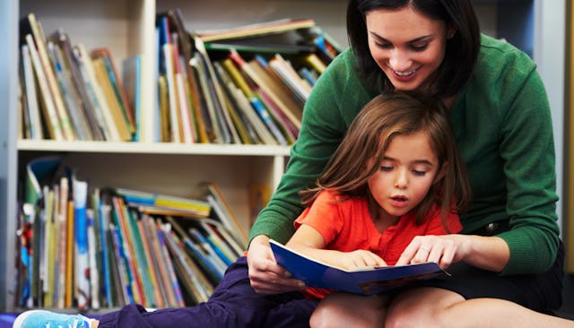 A kindergarten teacher sitting on a floor with a child reading a book