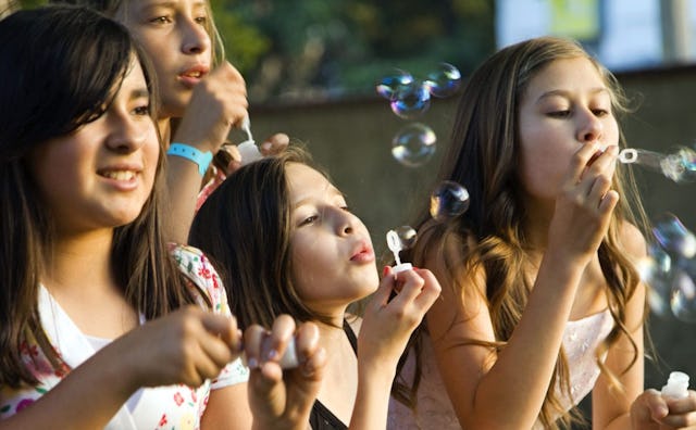 Four tween female friends making soap bubbles