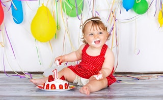 Baby enjoying her 1st birthday party with cake and balloons