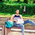 College-aged son laying on a bench with his laptop at the park