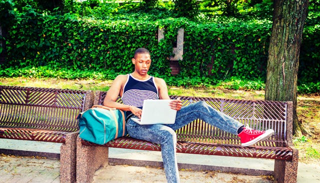 College-aged son laying on a bench with his laptop at the park