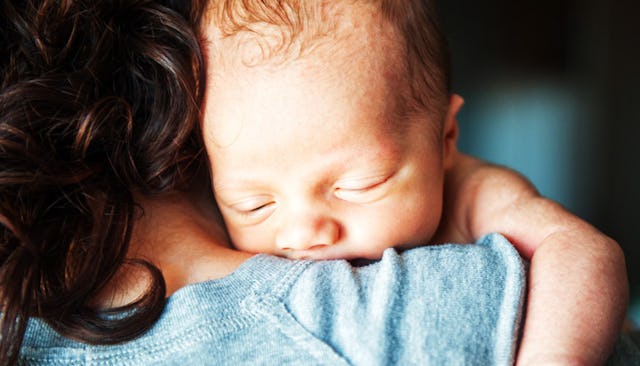 A mother holding her newborn sleeping baby on her shoulder