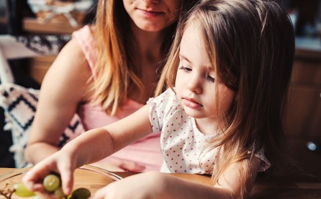 A little girl eating grapes while sitting in her mom's lap