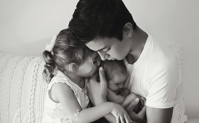 A teenage boy, lovingly embracing his two younger siblings, a toddler girl, and an infant