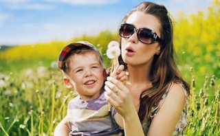 A mother and her son sitting in a meadow, blowing dandelions as divorce has made her a better mommy