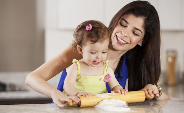 A babysitter is making dough in the kitchen with a smiling little girl.