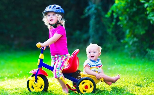 A toddler on a tricycle with a baby in the back of it.