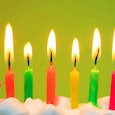 Ten candles in bright colors: pink, green, yellow, and orange, burning on top of a white birthday ca...