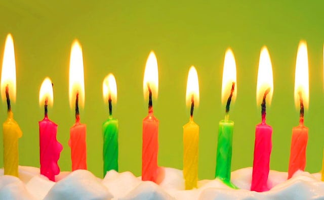 Ten candles in bright colors: pink, green, yellow, and orange, burning on top of a white birthday ca...